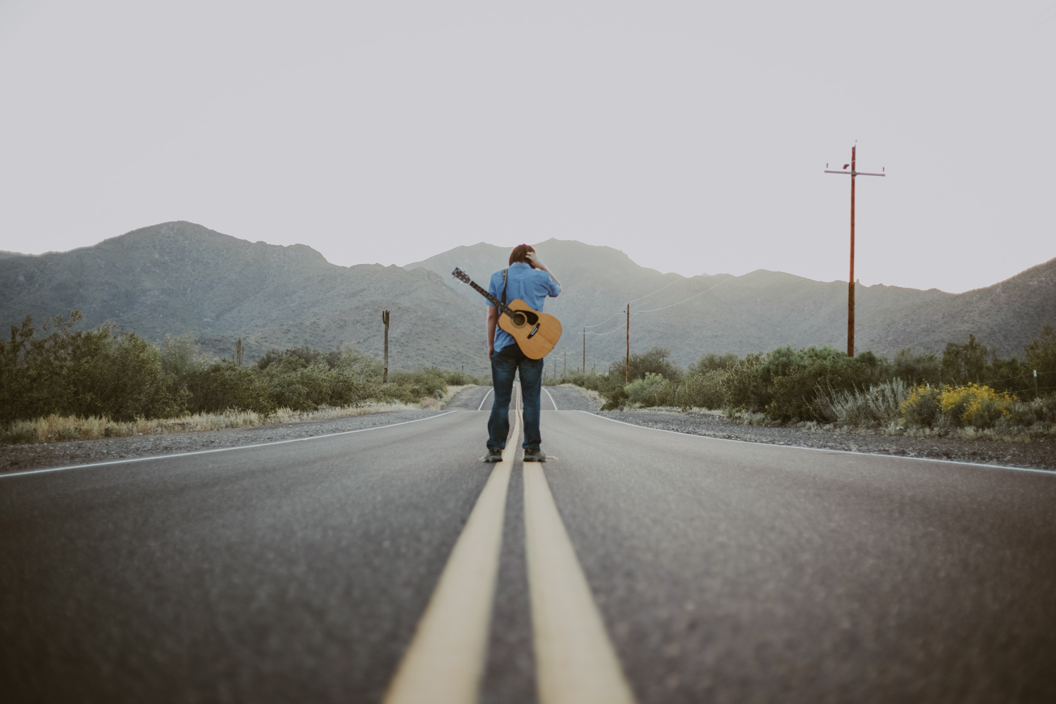 professional-branding-photographer-Advertising-photography-imagery-in-west-phoenix-arizona-with-young-musician-hitch-hiking-his-way-to-stardom-with-white-tank-mountains-in-the-background