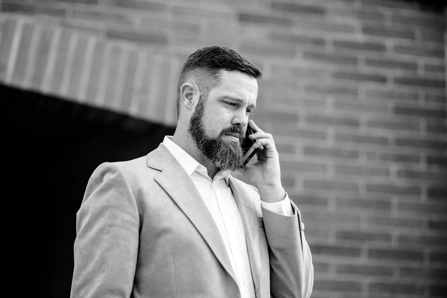 middle aged business man talking on cell phone important call suit jacket no tie beard black and white with brick backdrop coming out of tunnel personal brand financial advisor memphis tennessee by prefocus solutions