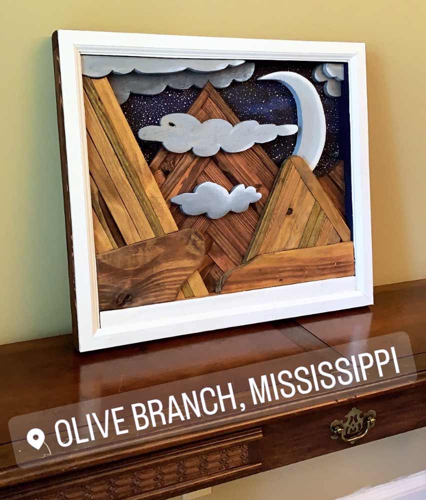 creative wooden wall art of trim pieces stained to look like mountains and different shapes of lumber cut to paint picture of crescent moonlit night sky stacked for effect and white trim with mahogany and oak finish sitting on dining room table by coarse grain near memphis
