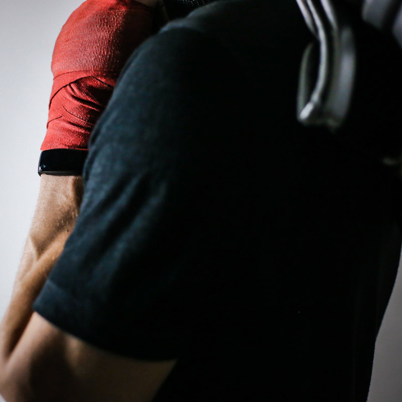 original image of boxing model holding gloves over shoulder with red wraps on and black fitness tracking watch shadow lighting for quality display ad design strategy  