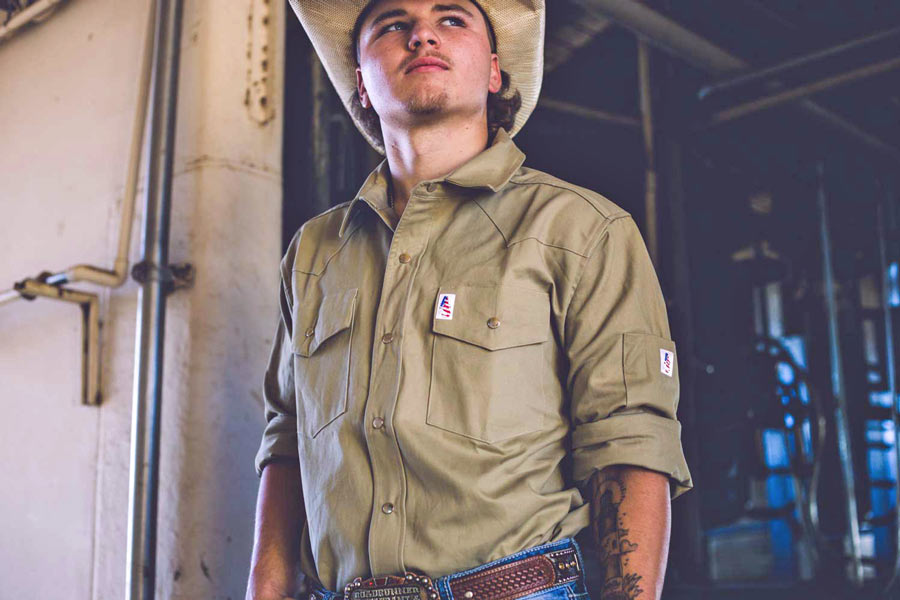 leaning against wall of pasteurizing building at local farm near memphis tennessee khaki cowboy shirt company straw hat creative strategy by jordan trask of prefocus solutions