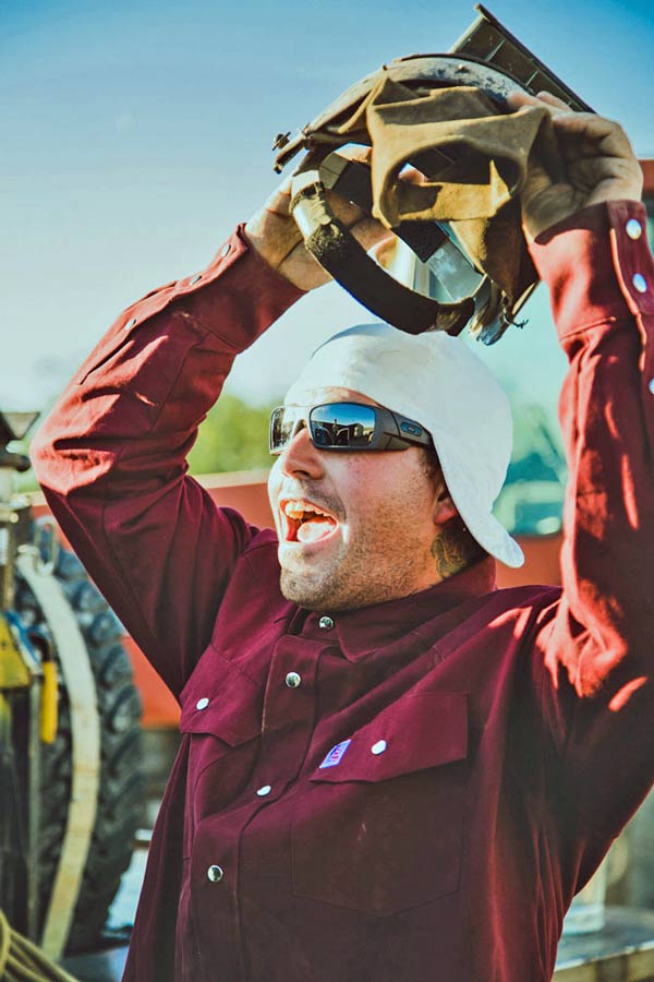 taking off welding helmet to yell at buddy across the work yard after long hard days work in memphis tennessee with creative director jordan trask for quality clothing line strategy